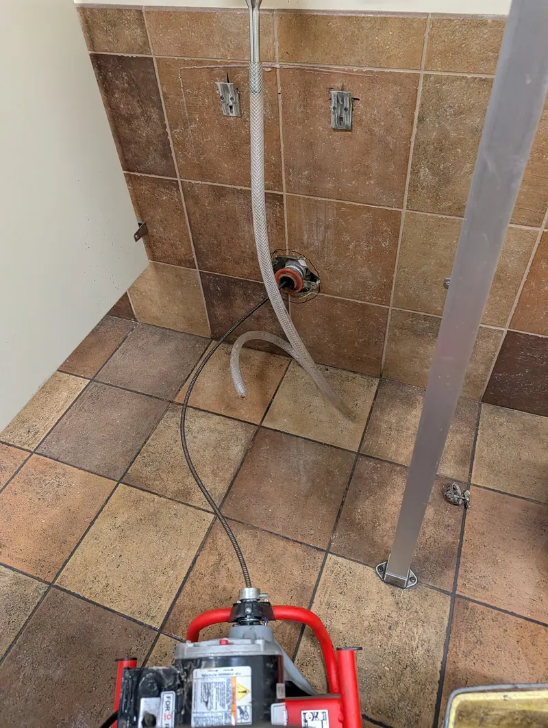 Drain machine set up to clear a floor drain in a tiled commercial restroom