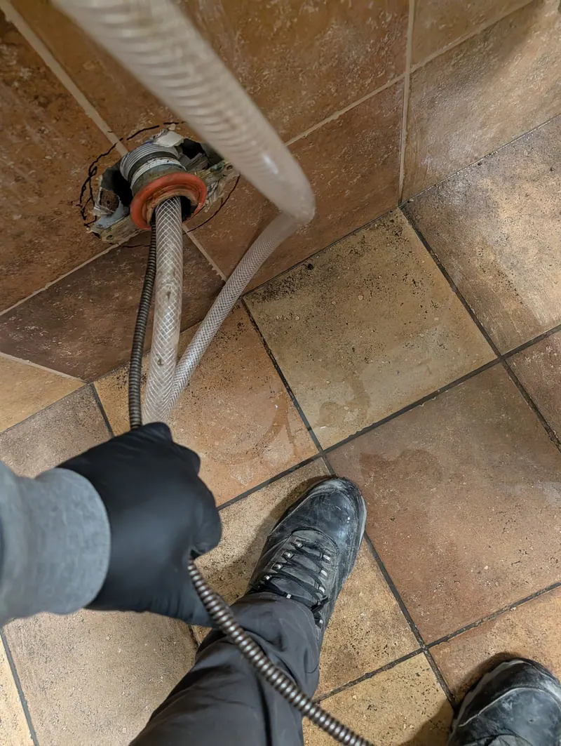 Fullerton plumber in work gloves feeding a drain cleaning cable into a floor drain